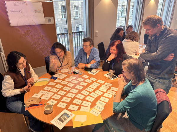 Teilnehmende des Workshops sitzen an einem Runden Tisch, auf dem Karten liegen.
