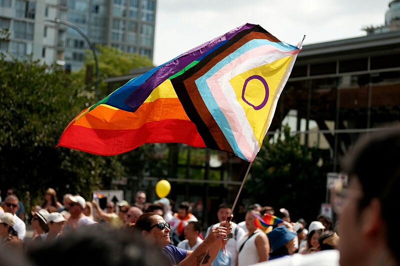Person hält eine Pride-Flagge mit Intersex-Inklusion über einer Menschenmenge bei einer Pride-Demonstration in einer Stadt.